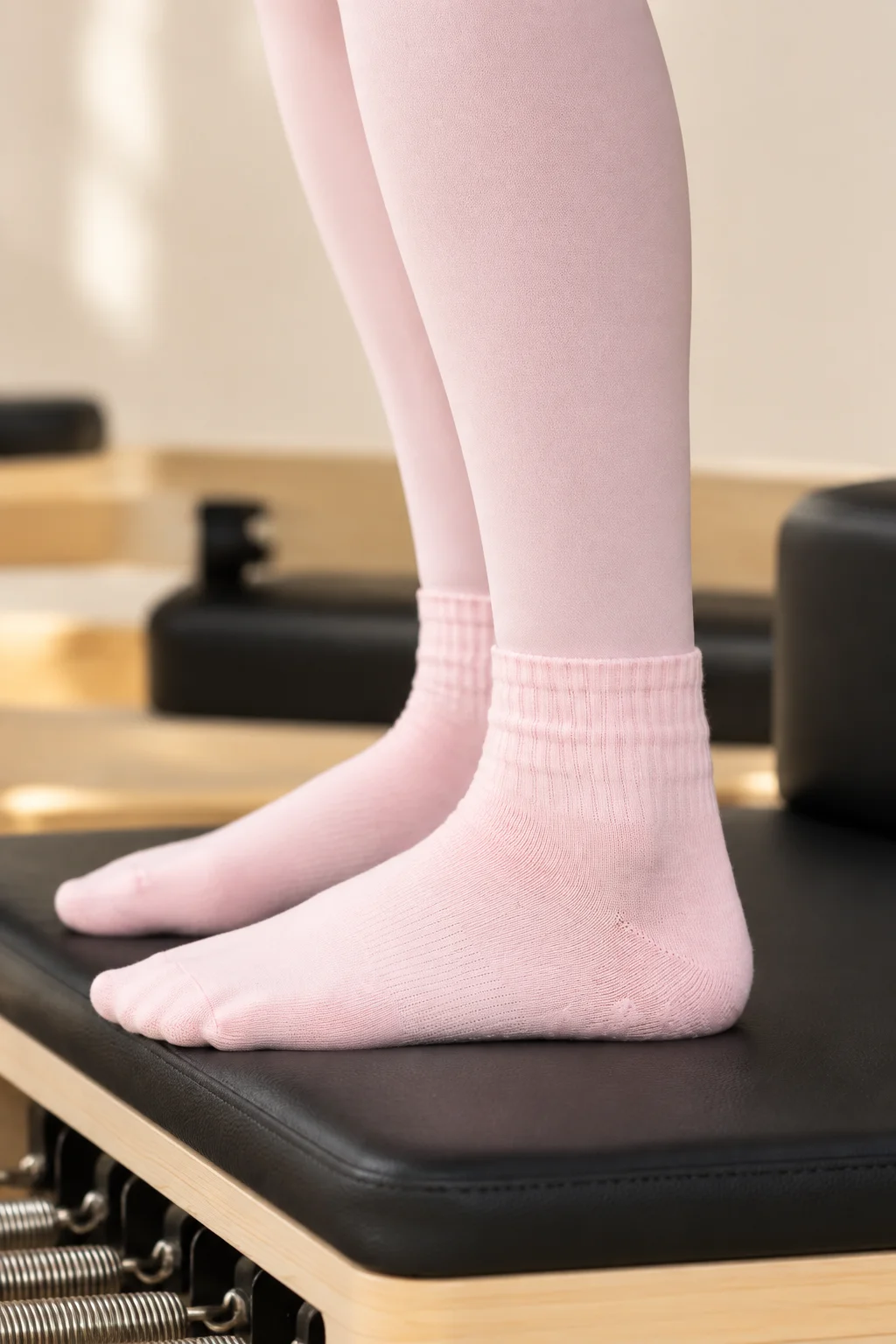 Voeten in roze sokken en een lichtroze legging op het zwarte kussen van een reformer